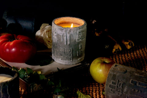 Candle in a rustic stone holder surrounded by fruits and vegetables on a dark background